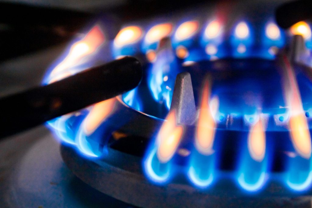 A gas burner ring seen close and low, the flames blue at the port with orange tips above