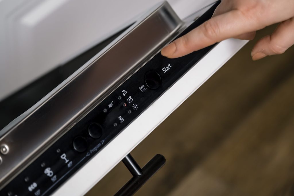 A finger pressing a control on the strip along the top edge of an open dishwasher door