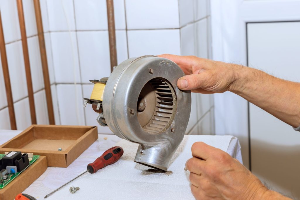 Two hands turning a stainless blower housing on a workbench with a screwdriver beside it