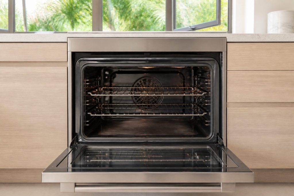 An empty built-in oven standing open in a bright kitchen with its racks in place