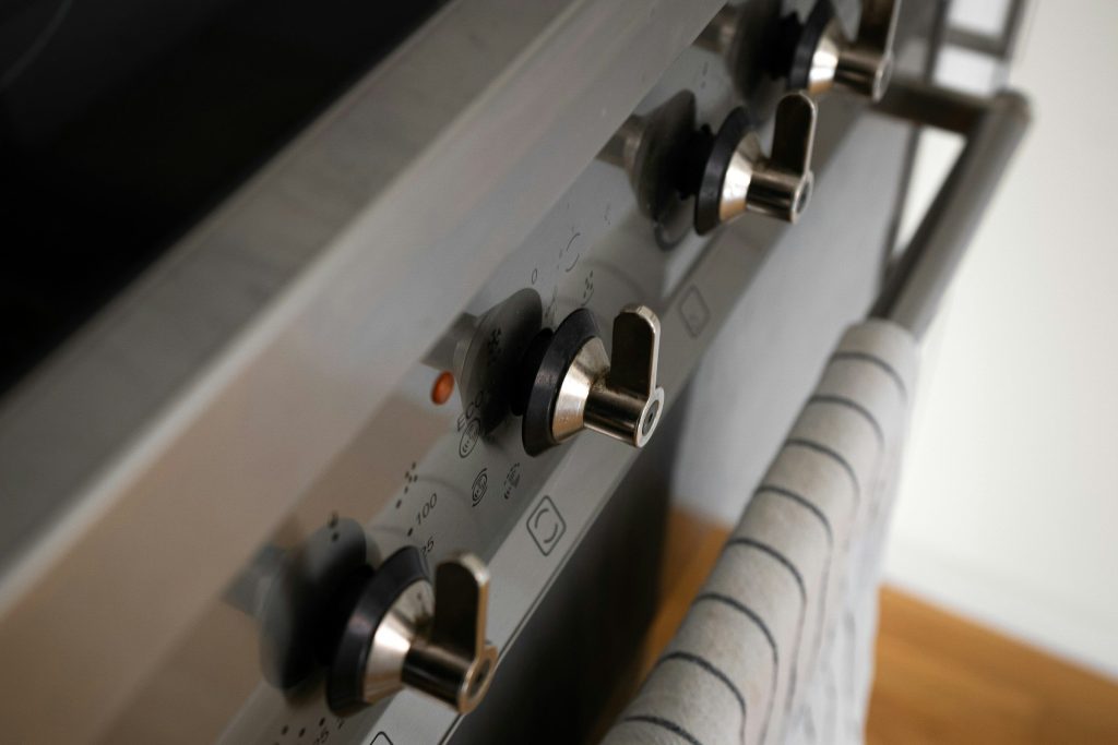 A row of metal control knobs along the front of a stainless range with one small indicator lit