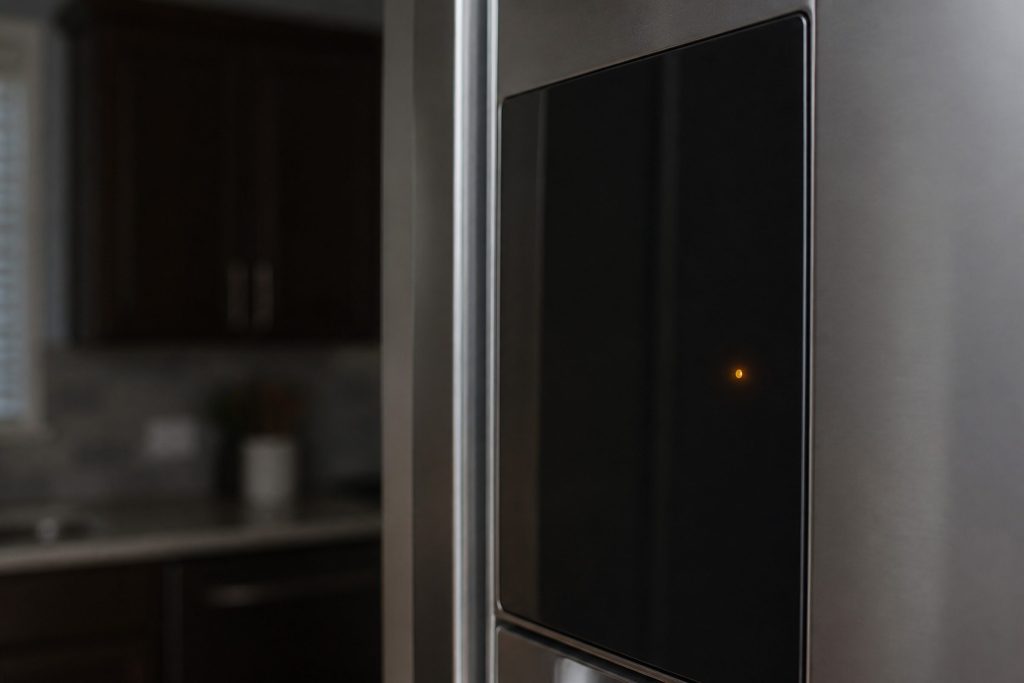 A tall refrigerator in a dim kitchen with a single small indicator lit on its door