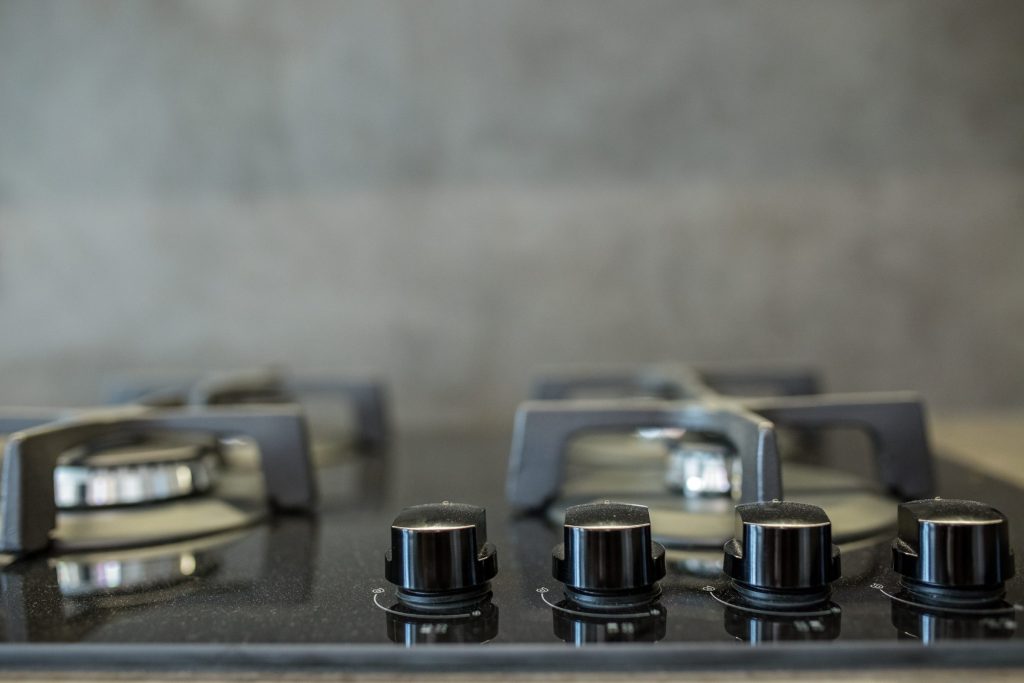 A row of dark metal control knobs along the front of a gas cooktop, the burner grates behind them out of focus