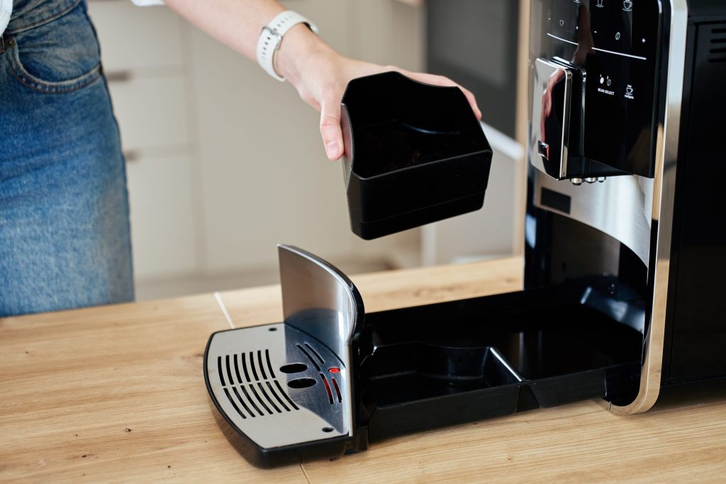 A hand drawing the waste container out of the open front of a built-in coffee machine