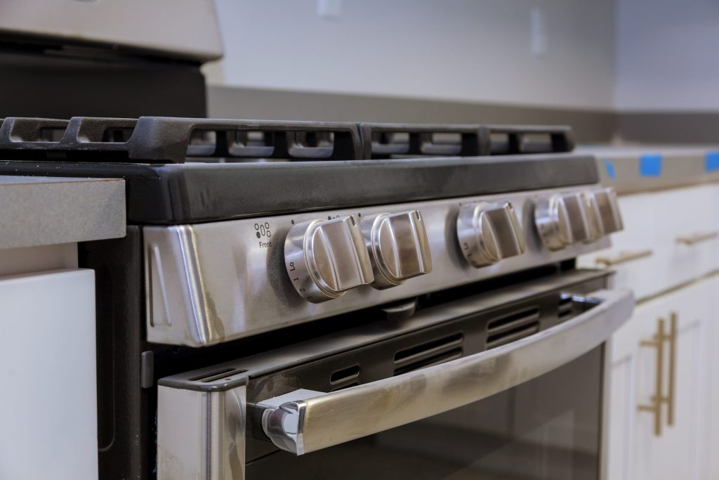The control fascia of a stainless dual-fuel range, its row of metal knobs and the oven door handle below