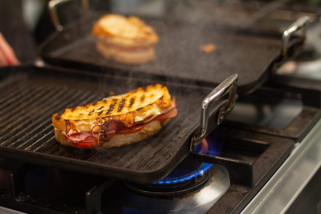 A heavy cast-iron griddle plate over a blue gas flame with food cooking on its ridged surface