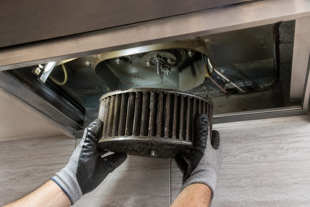 Gloved hands holding a grease-loaded blower wheel taken out from under a range hood