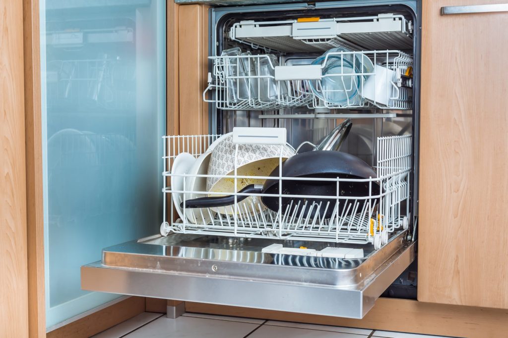 An integrated dishwasher standing open in a wood kitchen with dishes loaded in both baskets