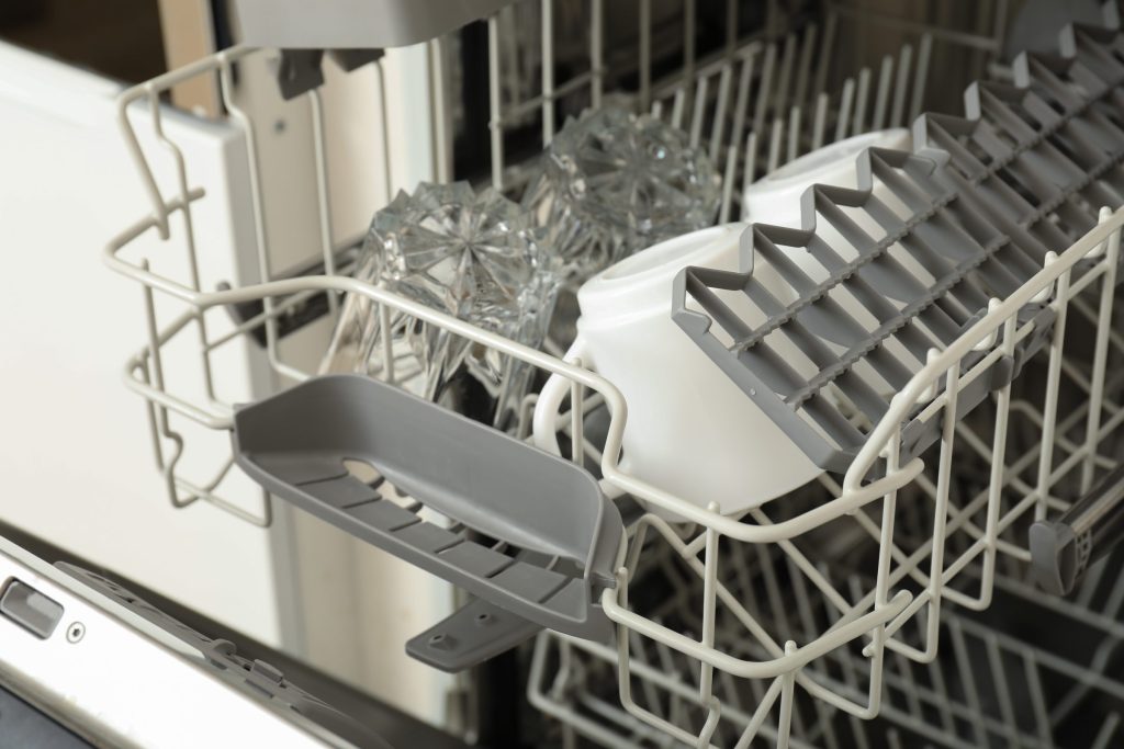 The lower basket of an open dishwasher with glasses in it and the tub floor visible below