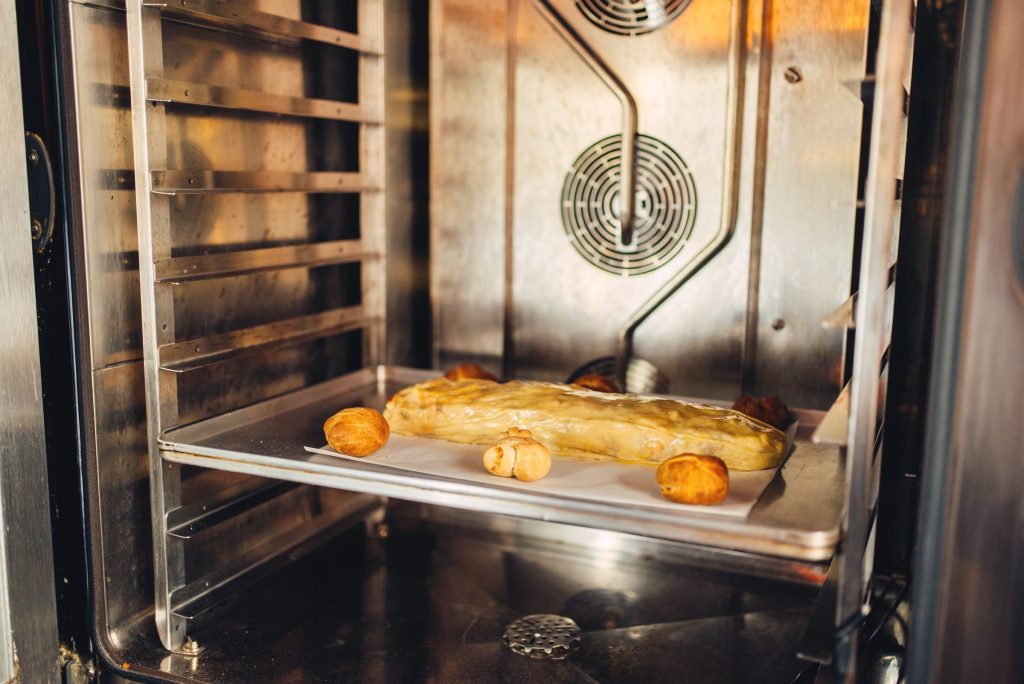 Looking into an open oven at a tray of part-baked pastries with the bake element visible at the back