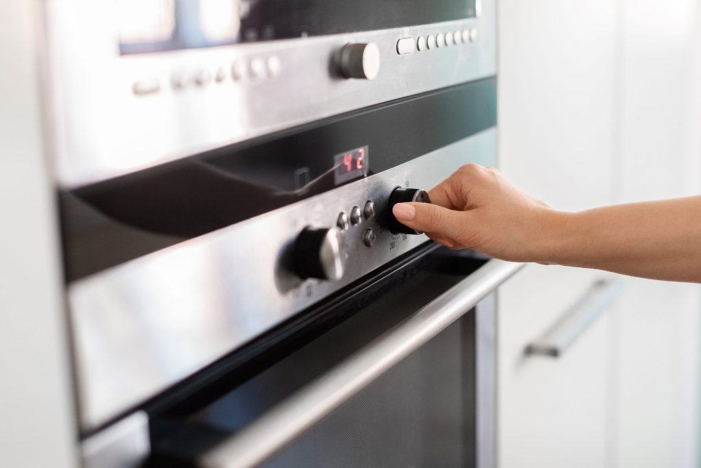 A hand turning the temperature knob on a built-in oven while the small display shows a set temperature