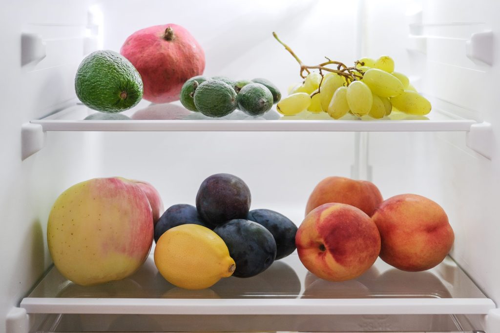 Fruit and vegetables on the glass shelves of a refrigerator with the interior light on