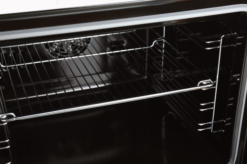 The inside of a cold oven with the circular convection fan cover on the rear wall behind empty racks
