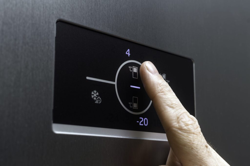 A finger on the temperature control panel of a refrigerator door, the display showing the two compartment settings
